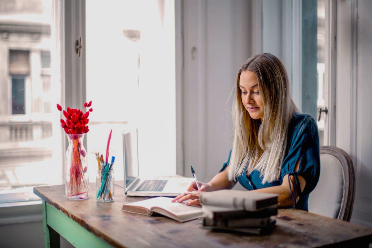 Frau arbeitet im Homeoffice an einem Schreibtisch mit Laptop und Notizbuch